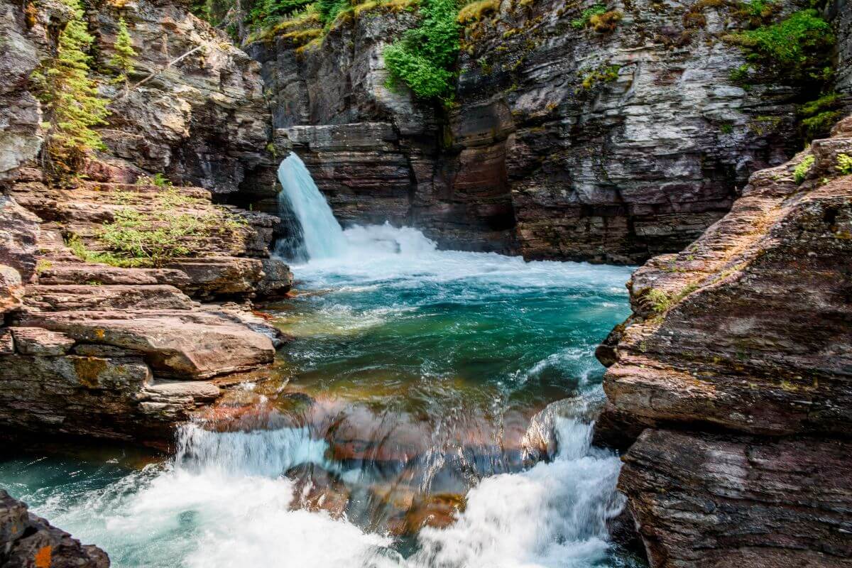 St. Mary Falls cascades down a rocky river as seen from a nearby trail