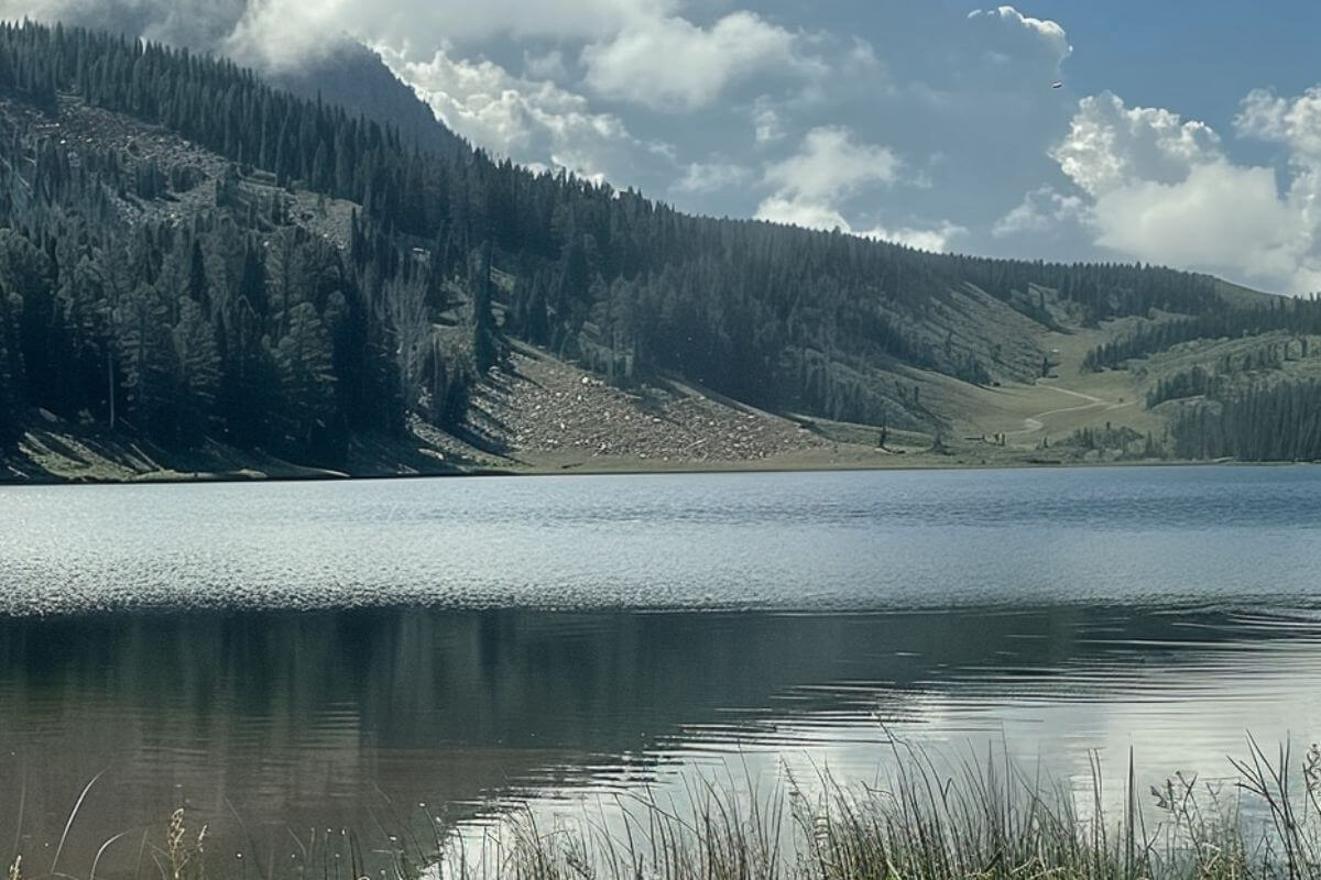 Stony Lake has clear, calm water reflecting pine-covered hills. The sky is partly cloudy with some blue patches.