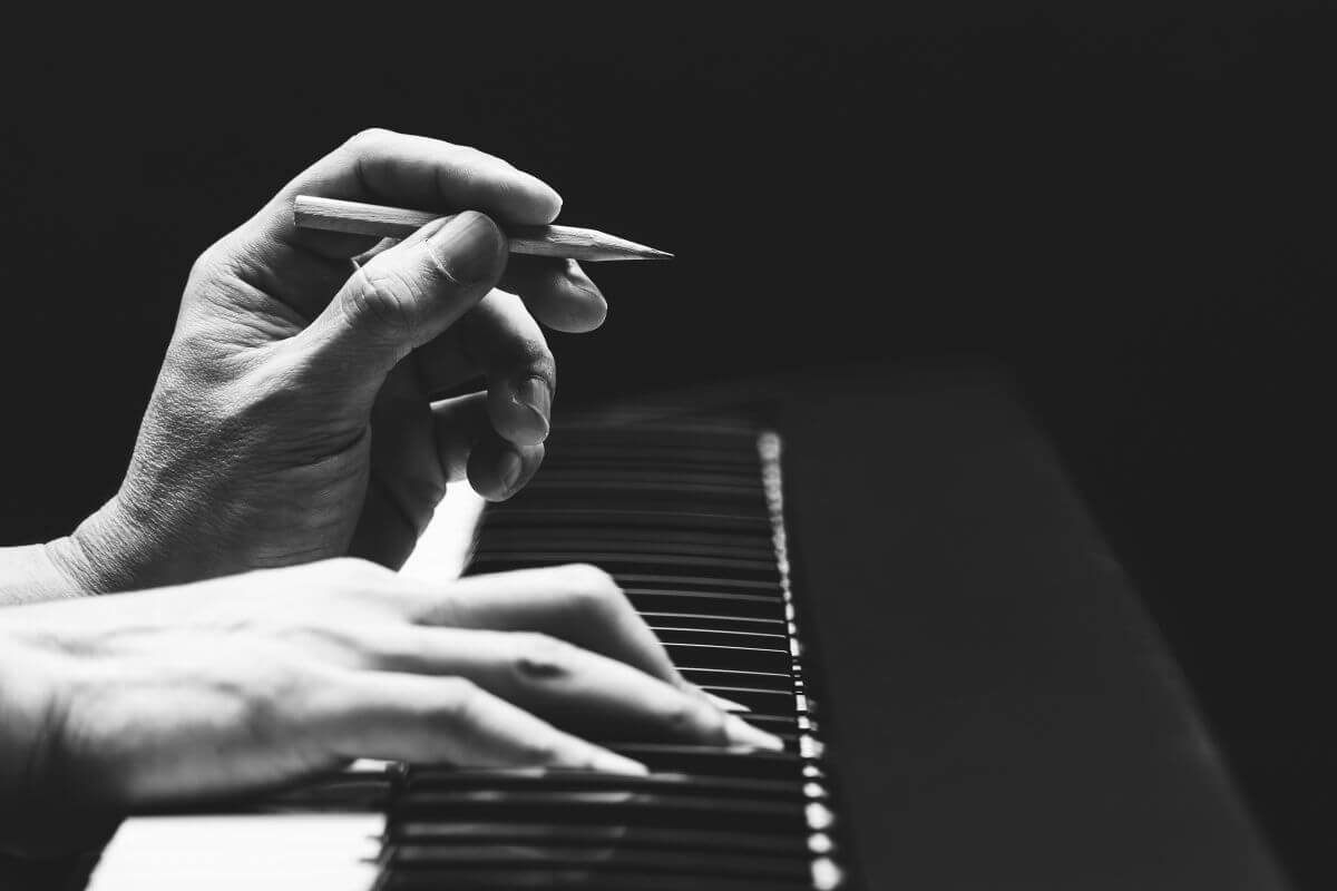 One Hand on the Piano and Another Hand Holding a Pencil